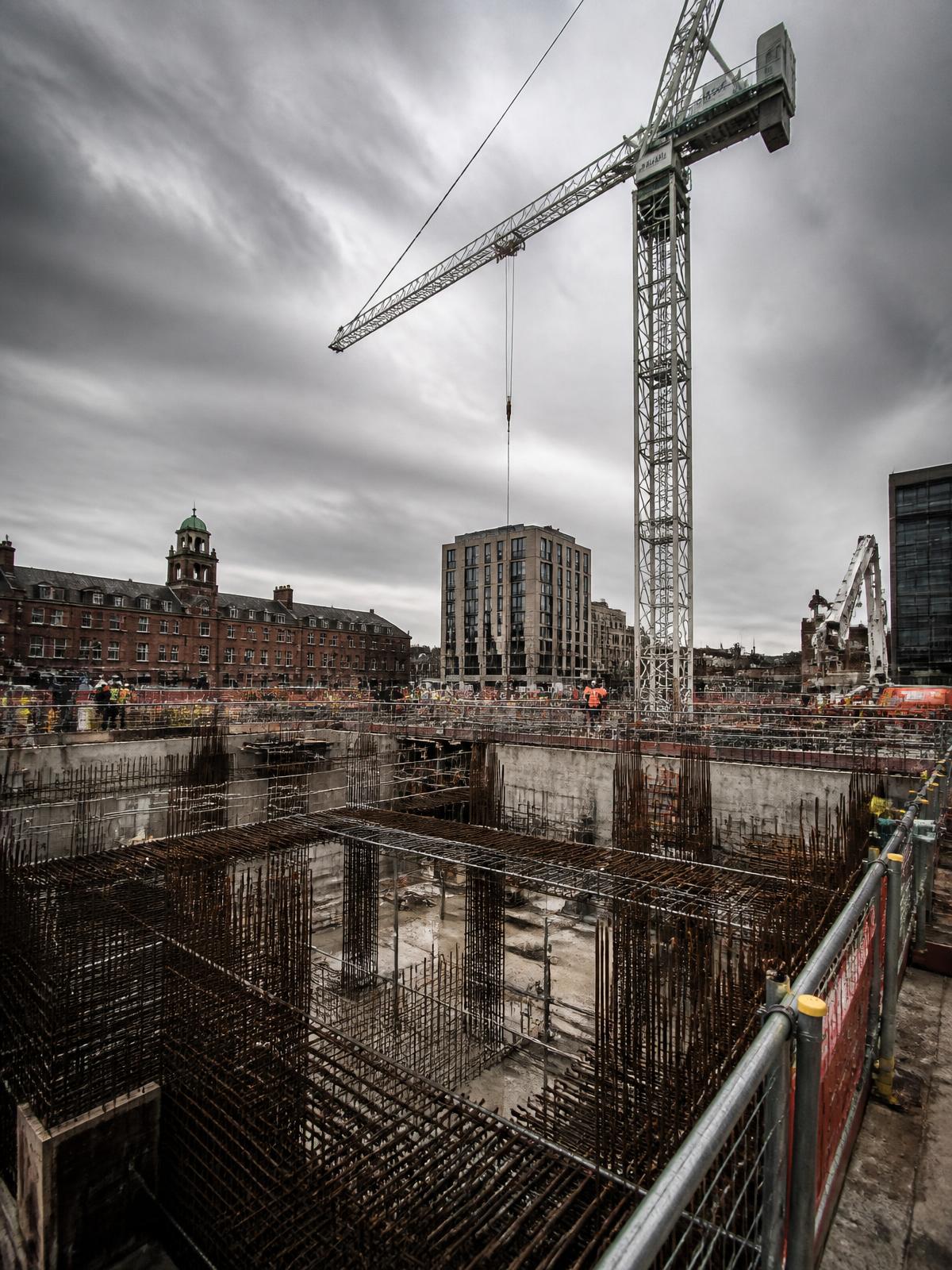 Deep concrete foundation excavation with exposed reinforcement on a large development site